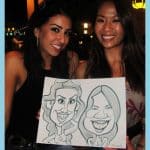Two smiling girls proudly holding their caricature drawing by artist Grant at an event.